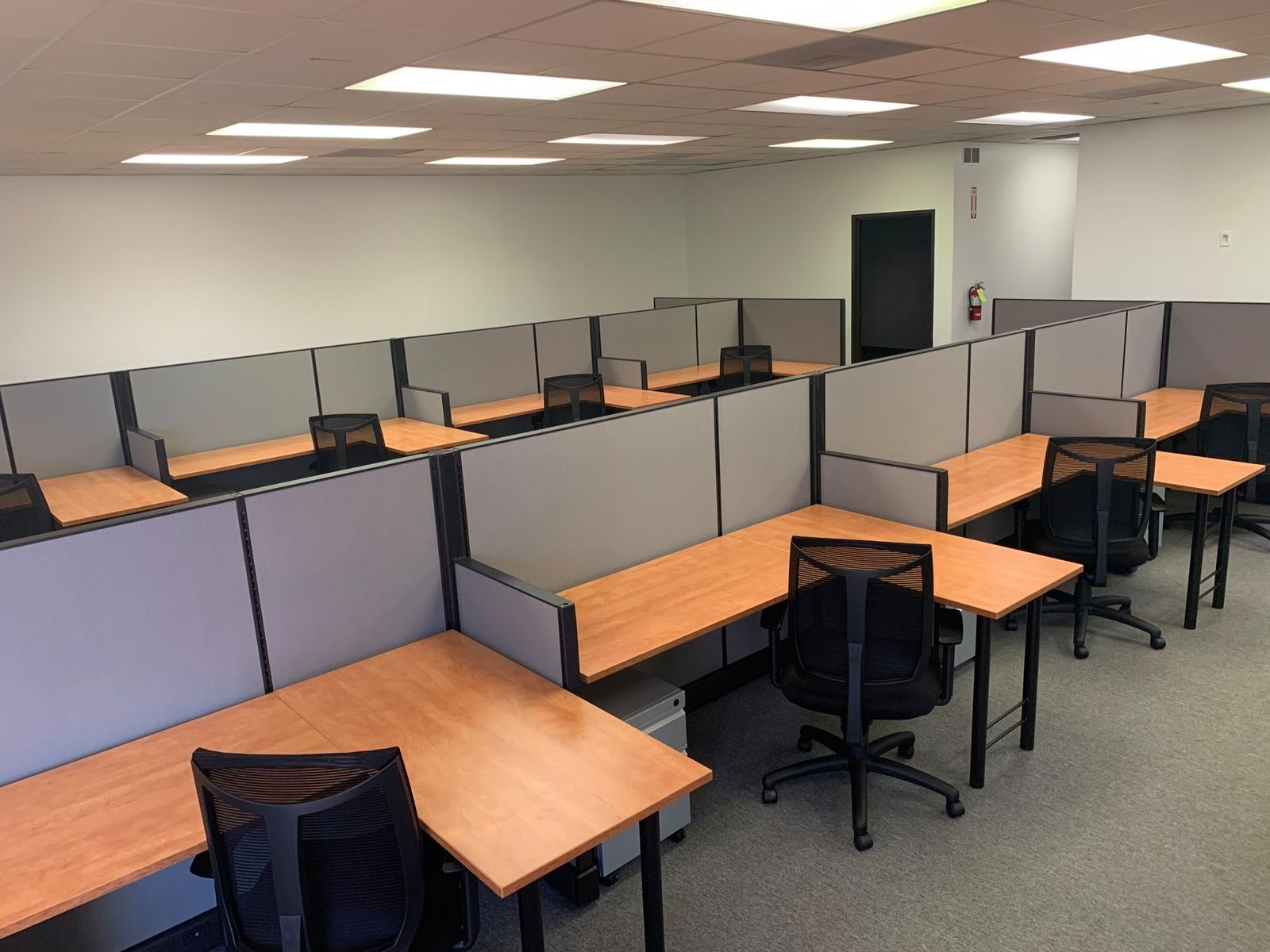 Rows of cubicle workstations with maple work surfaces and mesh task chairs, installed by Eggleston Office in an open office